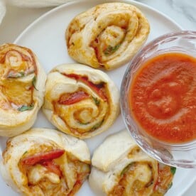 Pizza pinwheels on a plate with a side of marinara sauce