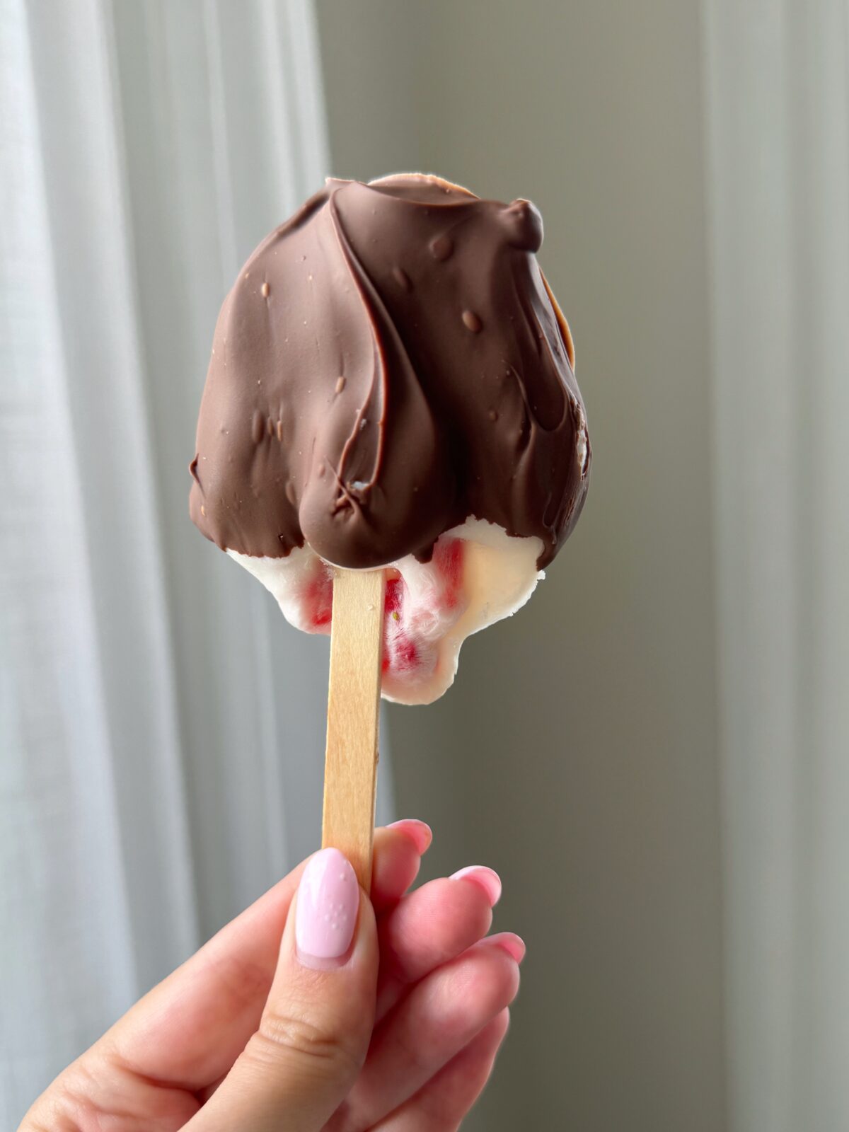 A hand holding a strawberry yogurt chocolate popsicle
